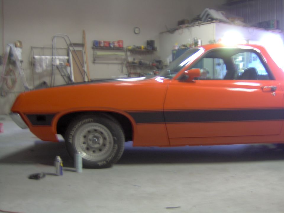 Orange car with black side stripe up on a wheel dolly in a garage, mid-restoration