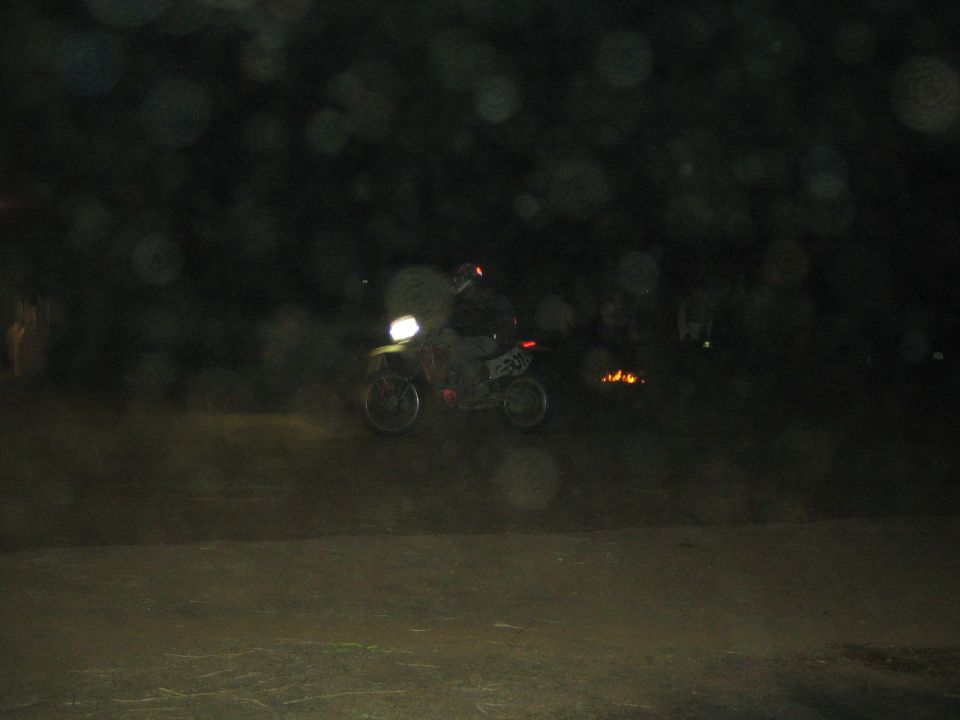 Dimly lit rider on a dirt bike with headlight on at a dark night event