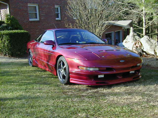 Red 1994 Ford Probe parked on grass in front of a brick house