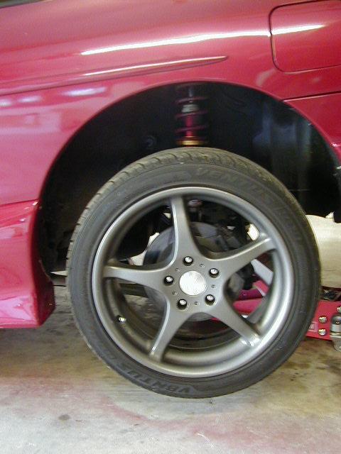 1994 Ford Probe - Close-up of a red car's rear wheel assembly, showing the tire, alloy rim, and suspension.