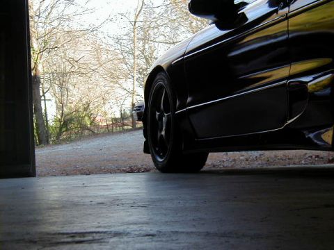 1994 Ford Probe - Side view of a black car with aftermarket wheels, partially in a garage.