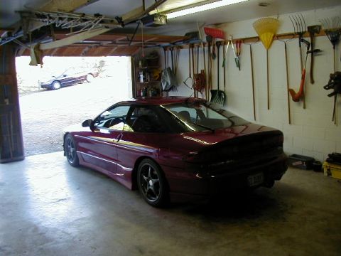 1994 Ford Probe - A maroon 1994 Ford Probe is parked in a garage, with gardening tools hanging on the wall and another vehicle visible outside.