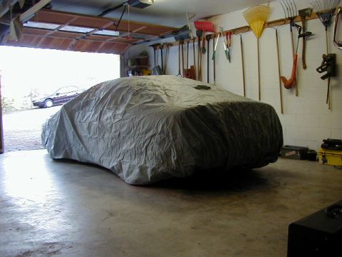 1994 Ford Probe - A car is covered by a gray car cover inside a garage, with tools hanging on the wall.