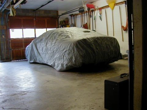 1994 Ford Probe - A car sits covered in a garage, with gardening tools hanging on the wall.