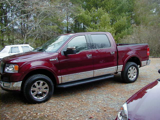 Red Ford F-150 pickup truck parked outdoors, with a white sedan in the background and part of another vehicle in the foreground