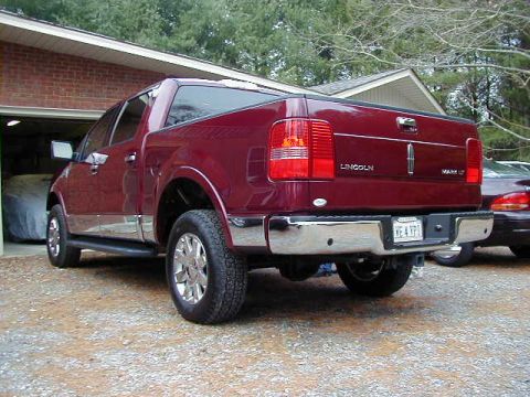 1994 Ford Probe - A red Lincoln pickup truck is parked in front of a garage, with another vehicle visible behind it.