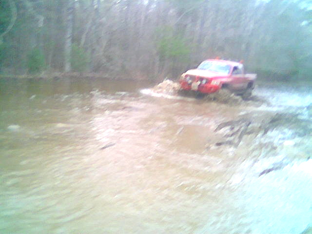 red pickup truck splashing through a muddy water crossing