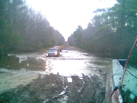 1976 GMC C/K Pickup - A truck navigates a challenging muddy road, with another vehicle visible ahead and the perspective from a second truck.