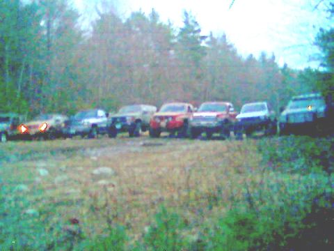 1976 GMC C/K Pickup - Multiple pickup trucks and SUVs are parked in a grassy area with trees in the background.