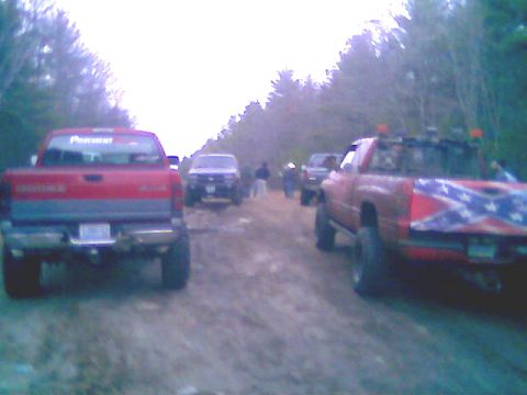 1976 GMC C/K Pickup - Multiple pickup trucks are seen on a dirt road, with one truck displaying a Confederate flag.