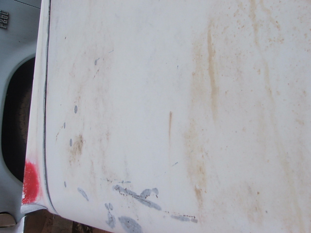 Close-up of a white vehicle door with rust stains and some gray primer