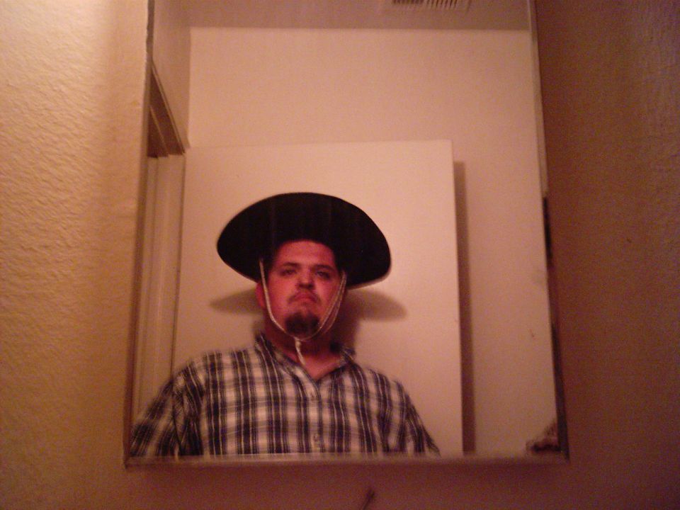 Man wearing a wide-brimmed hat and plaid shirt, reflected in a mirror