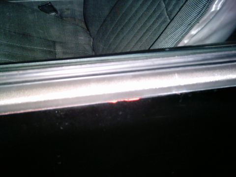 1986 Ford Bronco - Close-up view of a vehicle's interior door panel and seat, showing a small chip of red paint on the door frame.