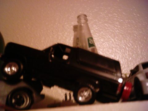 1986 Ford Bronco - A black SUV model is displayed on a shelf next to bottles, with another vehicle partially visible in the background.