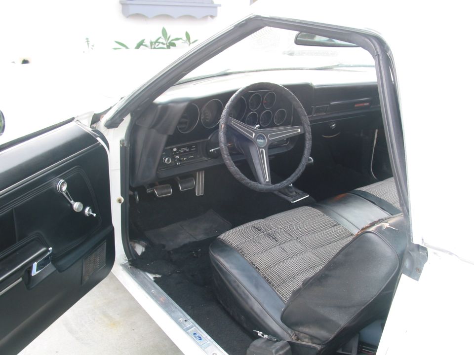 White 1972 Ford Ranchero interior, driver's side door open, showing black and houndstooth seat, dashboard with round gauges, and steering wheel
