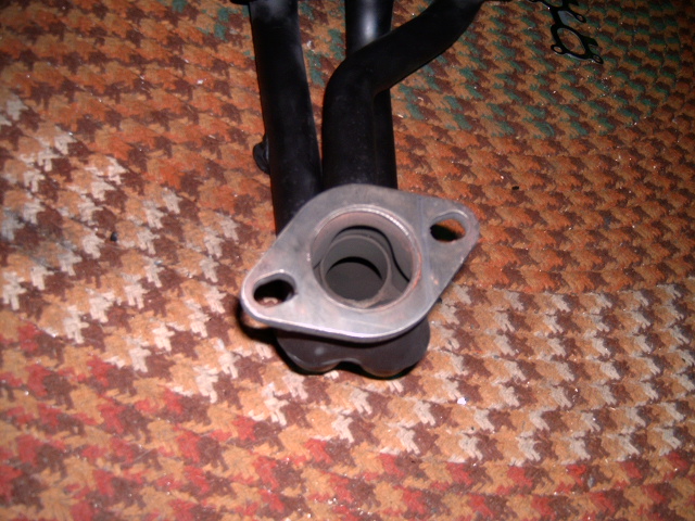 Exhaust manifold with two pipes and a flange, resting on a patterned carpet