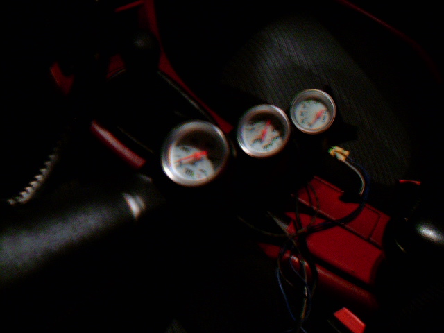 Three aftermarket gauges mounted on a red surface inside a vehicle