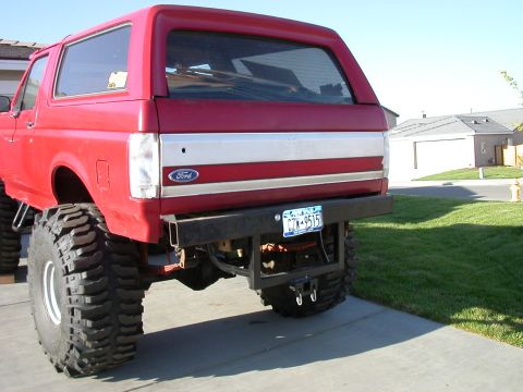 1991 Ford Bronco - Rear view of a red Ford Bronco, modified with large tires and an aftermarket bumper.