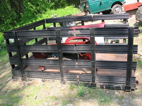 1985 Ford F-350 - A cage on a truck bed contains red car parts, with a green truck visible behind it.