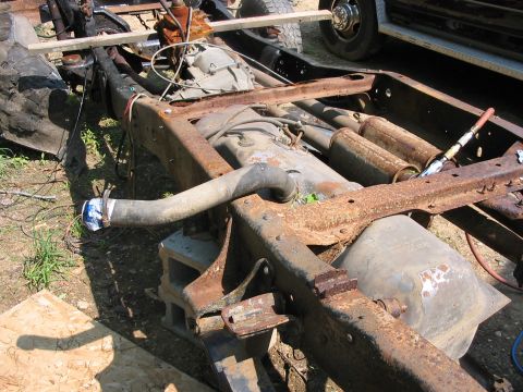 1985 Ford F-350 - The heavily corroded chassis of a truck is shown, with a fuel tank and dual exhaust pipes visible.