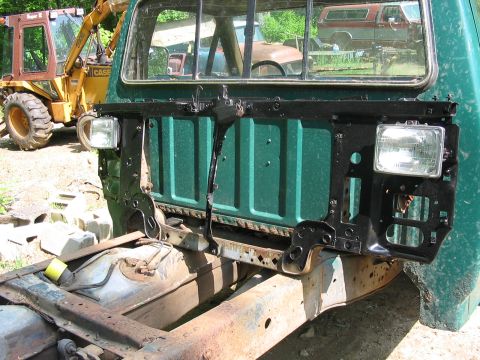 1985 Ford F-350 - The front end of a green truck is disassembled, revealing the chassis and fuel tank, with construction equipment nearby.
