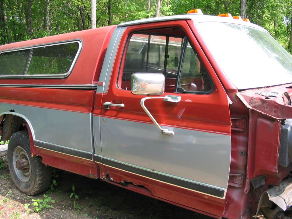 Red and silver pickup truck with a camper shell, showing significant rust on the lower body panels and missing the front fender