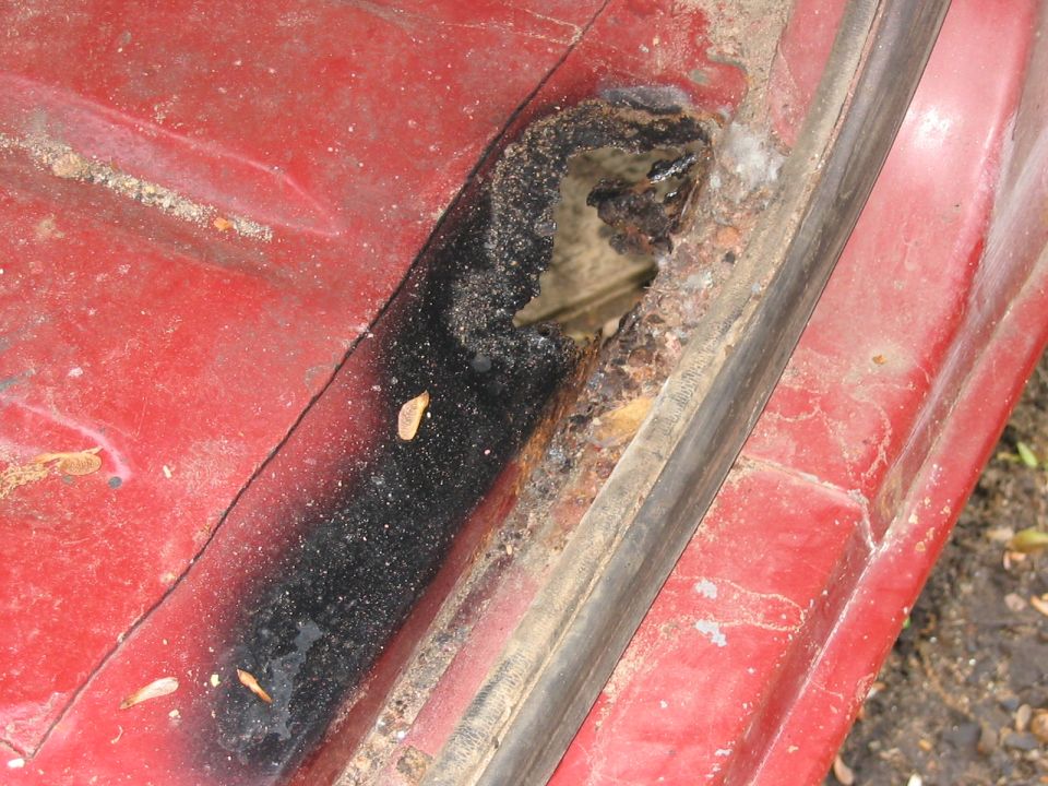 close-up of a hole with rust and water on a red vehicle panel