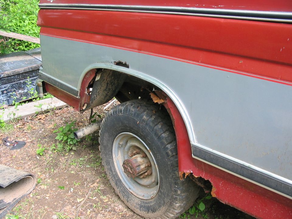 Rear fender and wheel well of a red and silver pickup truck with significant rust damage