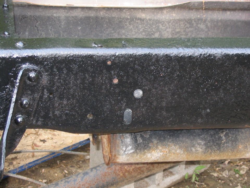 Black painted truck frame with visible rivets and bolt holes. Rusty exhaust pipe is visible below