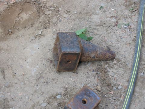 1985 Ford F-350 - Two heavily rusted metal brackets are lying on the dirt ground next to a green and yellow striped hose.