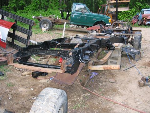 1985 Ford F-350 - A disassembled truck chassis is the main focus, with a green truck cab and other parts visible in the background.