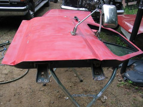 1985 Ford F-350 - A detached red truck door is propped up on a stand, with other vehicles visible in the background.
