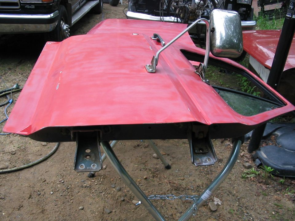 Red truck door with chrome mirror on a stand, other vehicles in background