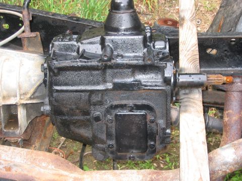 1985 Ford F-350 - A close-up view of a vehicle's transmission assembly, supported by wood, with visible rust on the frame.