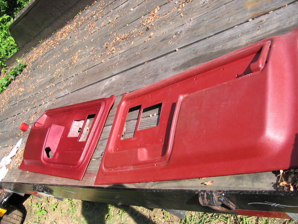 Two red plastic door panels with cutouts for window cranks and handles, lying on a wooden surface