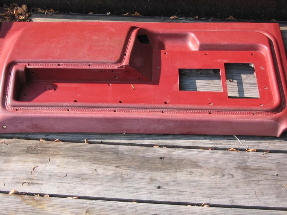 Red plastic door panel with cutouts for window crank and speaker, resting on wooden planks