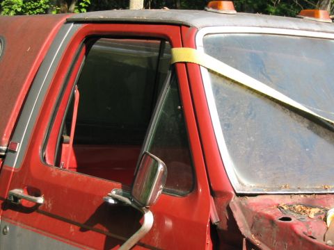 1985 Ford F-350 - A red and silver pickup truck cab is shown from the front passenger side, with a yellow strap securing the windshield.