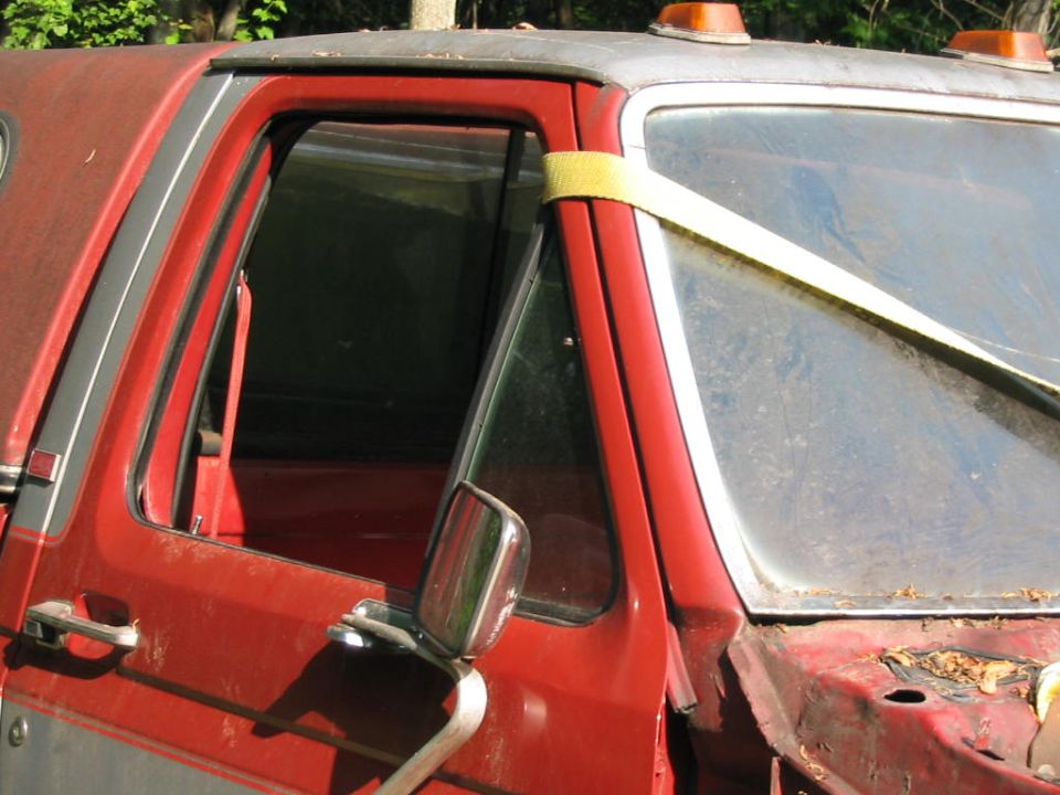 Red and silver pickup truck cab with a yellow strap across the windshield. The truck appears weathered