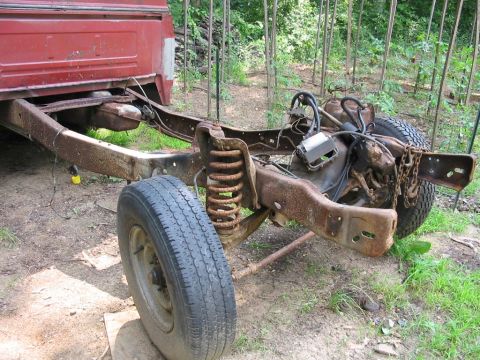 1985 Ford F-350 - A heavily rusted truck chassis, likely from the early 1980s, sits outdoors with its front suspension and engine exposed.