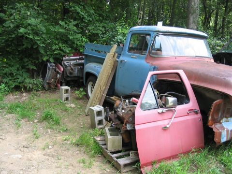 1985 Ford F-350 - Junkyard scene with two old pickup trucks and various engine parts, including a detached pink door.