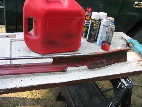 1985 Ford F-350 - Workbench setup with a red gas can, various spray cans, and a rusty car part, with a portion of a green vehicle visible.