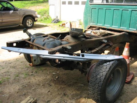 1985 Ford F-350 - Chassis of a green truck, showing the fuel tank and rear suspension, with a new bumper installed. An SUV is visible in the background.
