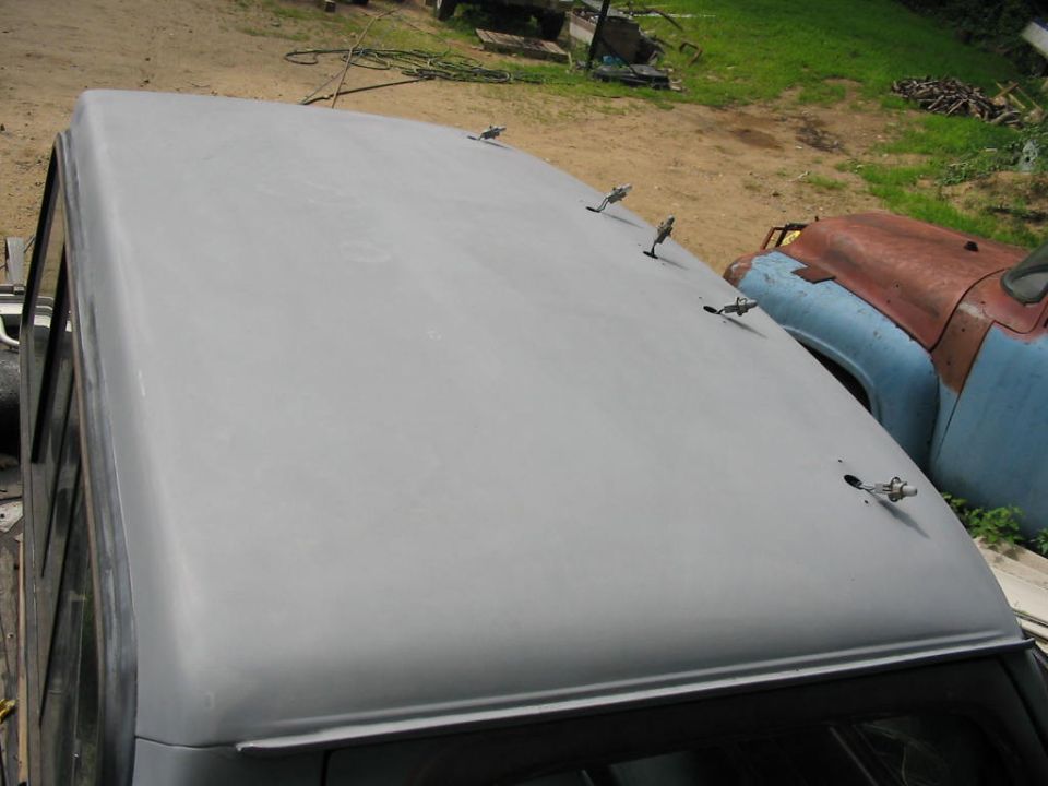 Gray primer-coated truck roof with several latches visible; another old truck in the background