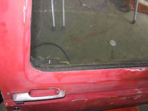 1985 Ford F-350 - Close-up of a red truck's side door and window, showing wear and tear.