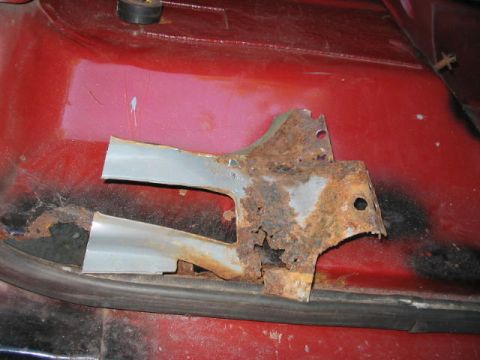 1985 Ford F-350 - Close-up view of a heavily rusted metal bracket attached to the red body of a vehicle, indicating wear and tear.