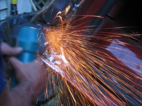 1985 Ford F-350 - A person uses a grinder, creating a shower of sparks on a red metal surface.