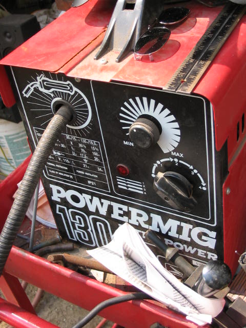 1985 Ford F-350 - Close-up of a red welding machine, identified as a POWERMIG 180, with various controls and a welding lead attached.
