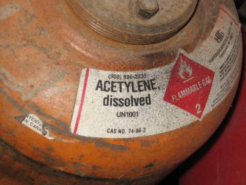 1985 Ford F-350 - Close-up of an orange acetylene gas cylinder, showing its "Flammable Gas" warning label and dissolved acetylene designation.