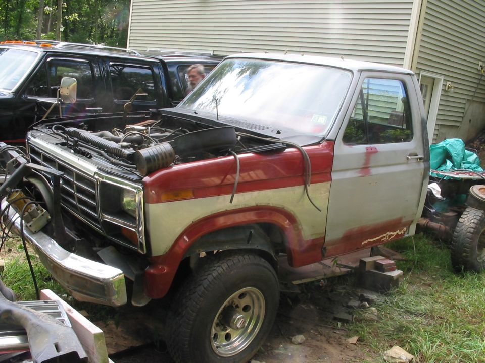 Front view of red and silver pickup truck with hood open, body style suggests 1980s Ford