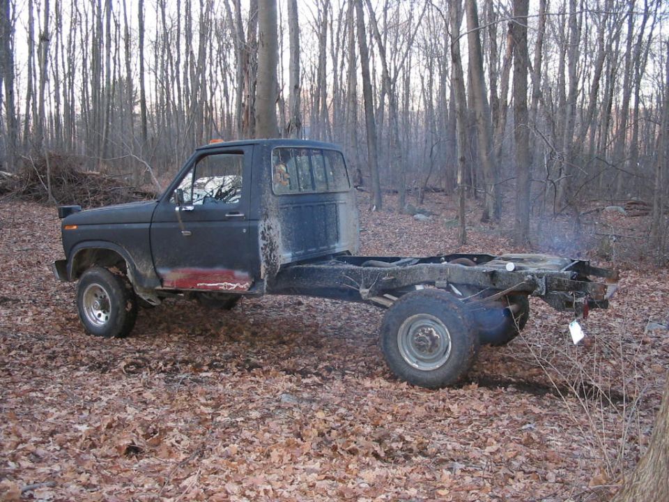Ford F-350 truck chassis with cab, missing bed, parked in woods